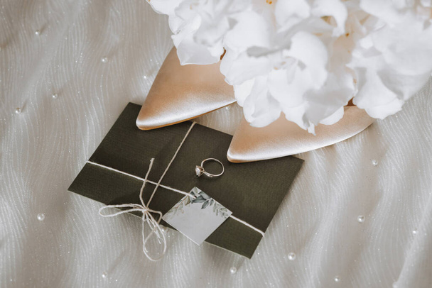 wedding accessories in light colors, shoes, a wedding ring and a wedding bouquet. Invitation from embossed paper in green color - Fotó, kép