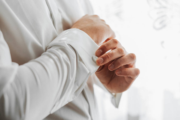Portrait of a fashionable man fastening stylish cufflinks on the sleeves of his white shirt. Wedding day concept. - Photo, Image
