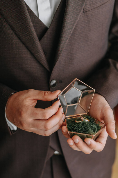 Wedding gold rings on a decorative glass box with wooden green moss, standing in the hands of the groom, close-up. Jewelry concept - Fotó, kép