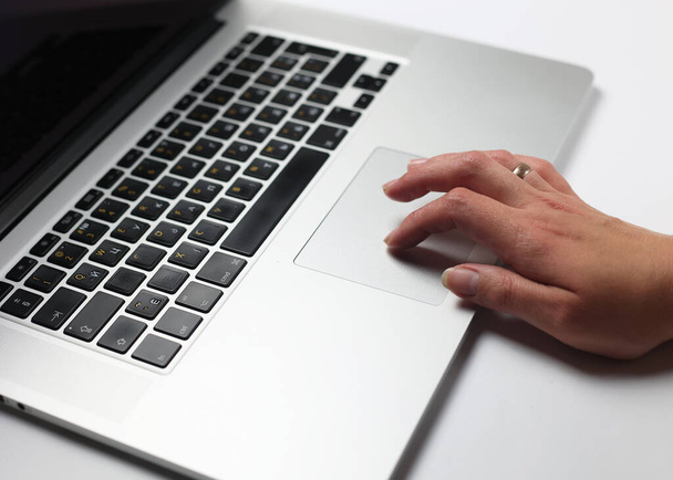Ένα φορητό υπολογιστή σε λευκό φόντο, ένα χέρι πιέζει τον πίνακα αφής. Κοντινό πλάνο ενός χεριού που δουλεύει με ένα λάπτοπ. Blogger στον υπολογιστή, ανεβάζοντας περιεχόμενο. Εργασία στο τραπέζι - Φωτογραφία, εικόνα