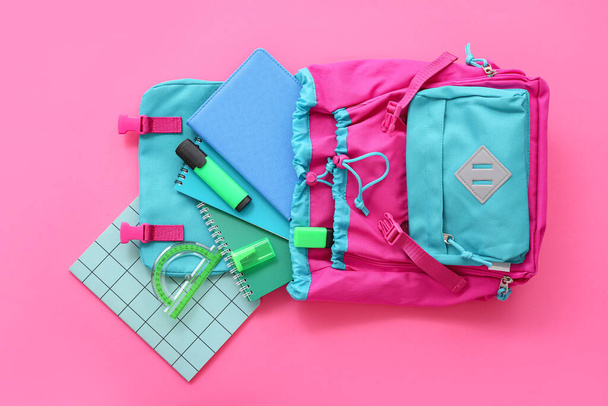 Color school backpack with notebooks, protractor and markers on pink background - Foto, afbeelding