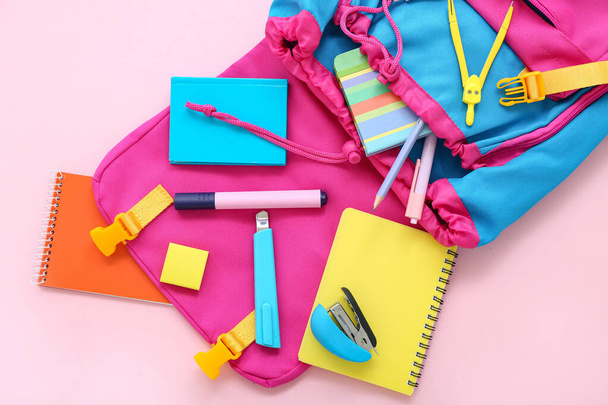 Рюкзак с блокнотами и канцелярскими принадлежностями на розовом фоне - Фото, изображение