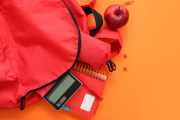 Mochila escolar roja con estuche de lápiz, calculadora y manzana sobre fondo naranja - Foto, Imagen