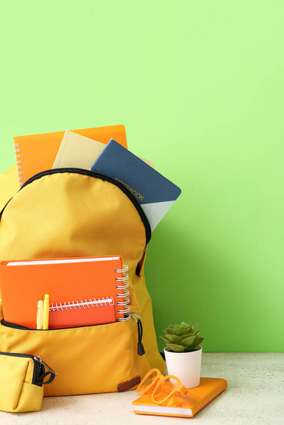 Sac à dos scolaire jaune avec carnets, étui à crayons et lunettes sur table grunge blanche près du mur vert - Photo, image