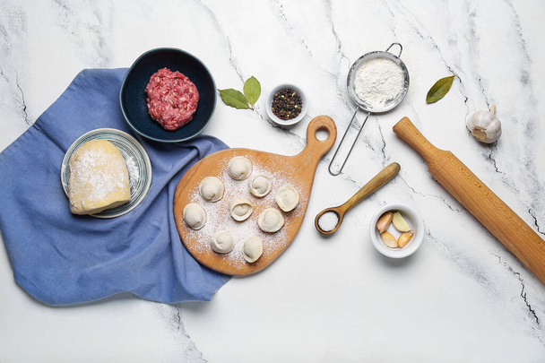 Houten bord met ongekookte knoedels en ingrediënten op witte marmeren ondergrond - Foto, afbeelding