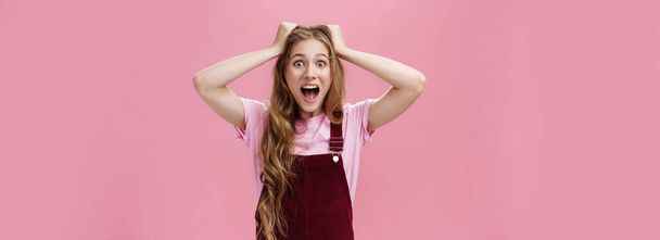Lifestyle. Female teenager cannot calm down feeling excited going on favorite band concert holding hands on head screaming from amazement and surprise standing overreacting against pink background. - Фото, изображение