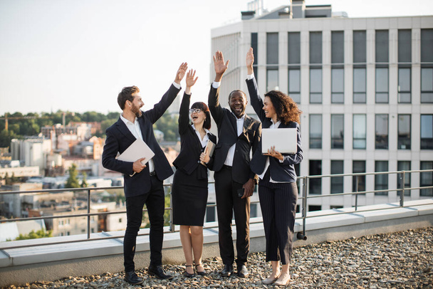Group of diverse colleagues celebrating shared corporate success and raising hands in air outdoors. Happy business partners enjoying moment after making great deal. Concept of teambuilding. - Fotoğraf, Görsel