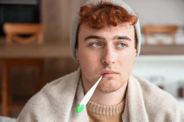 Kranker junger Mann misst zu Hause Temperatur mit Thermometer, Nahaufnahme - Foto, Bild