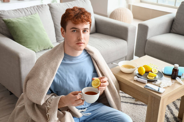 Młody człowiek pije herbatę z cytryną w domu. - Zdjęcie, obraz
