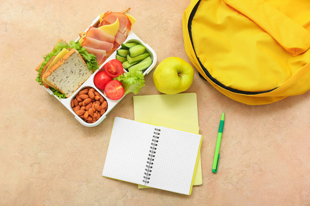 Backpack, stationery and lunch box with tasty food on grunge orange background - Foto, Imagen