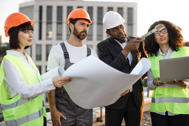 Diverse group of architects looking at construction diagram and discussing settlement of terraces on residential complex. African american woman holding portable laptop for entering data in program. - Foto, Bild