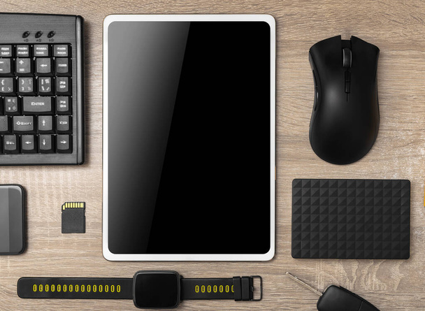 Tablet ordenador, smartphone, teclado, relojes inteligentes, ratón de la computadora en la mesa de madera. Vista desde arriba
. - Foto, imagen