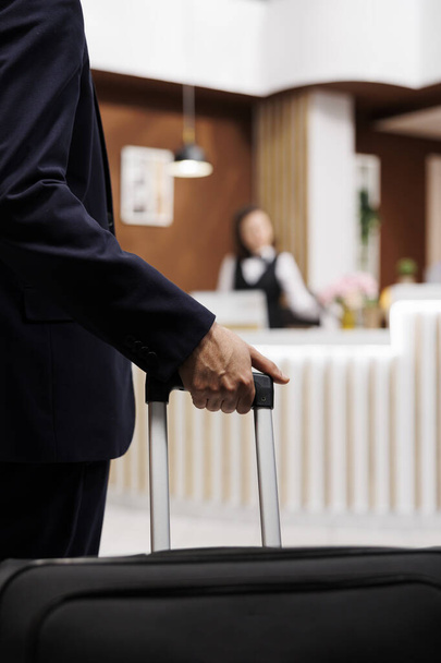 Hotel guest entering reception with luggage, travelling abroad to attend important business meetings. Entrepreneur approaching front desk for check in, booking accommodation. Close up. - Foto, afbeelding