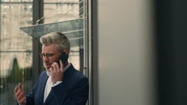 Vzteklý šílený agresivní úzkostlivý podrážděný zralý běloch argumentovat křičí mluvící telefon ve městě v blízkosti zdi kancelářské budovy stres starý podnikatel odpověď zavolat obchodní konflikt venku - Záběry, video