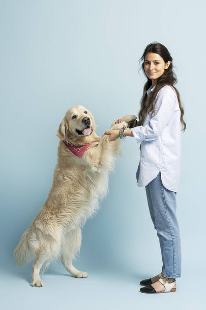 Beautiful golden labrador standing on its hind legs, being held by cute Latin woman looking at camera. Concept of animal care, active lifestyle - Photo, Image