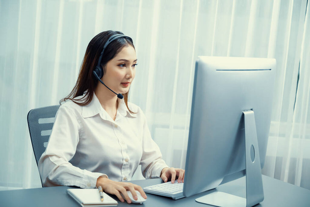 Asian call center with headset and microphone working on her laptop. Female operator provide exceptional customer service. Supportive call center agent helping customer on inquiry. Enthusiastic - Foto, Bild