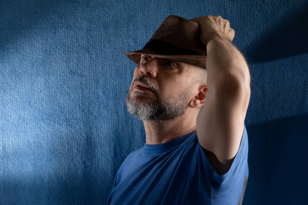 Retrato del estudio del hombre barbudo sosteniendo el sombrero sobre la cabeza. Aislado sobre fondo azul. - Foto, imagen