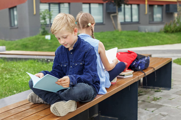 Children read books sitting on bench in school yard. Back to school. Beginning of school lessons. - 写真・画像