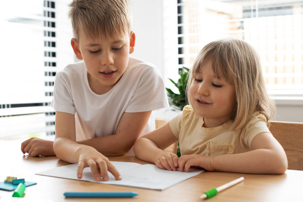 The older brother teaches the younger sister to read letters. The concept of brother and sister, home schooling. - Foto, Imagem