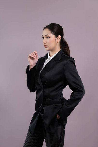 Confident young businesswoman stands on isolated background, posing in formal black suit. Office lady or manager with smart and professional appearance. Enthusiastic - Fotografie, Obrázek