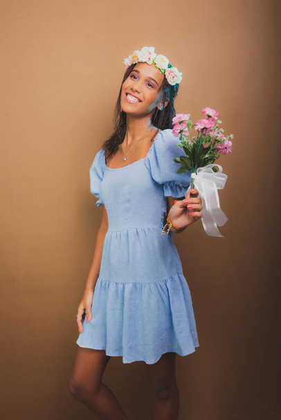 Retrato de una hermosa adolescente de pie sosteniendo ramo de flores. Aislado sobre fondo marrón. - Foto, Imagen