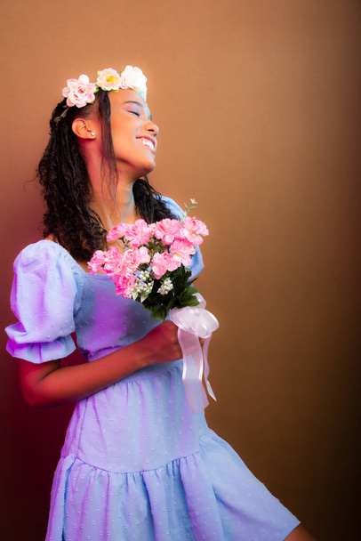 Portrait of beautiful girl, teenager, wearing blue, with tiara on her head and holding bouquet of flowers. Isolated on brown background. - Photo, image