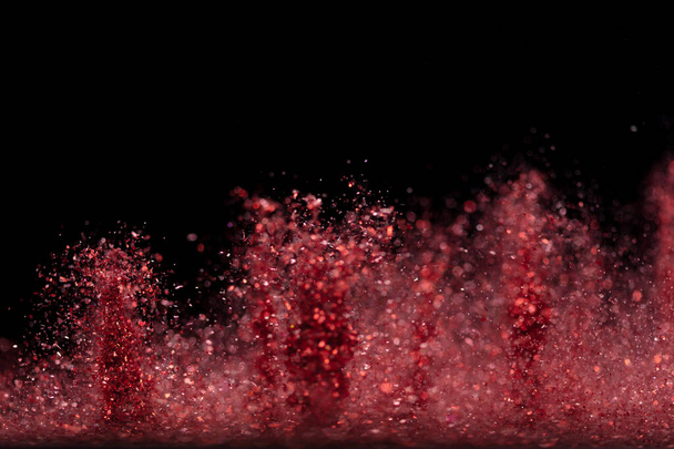 Взрыв металлического красного блеска сверкает. Розовый блеск пороха искры мигать праздновать, размытие фольги взорваться в воздухе, муха бросать красные блёстки частицы. Черный фон изолирован, селективный фокус - Фото, изображение