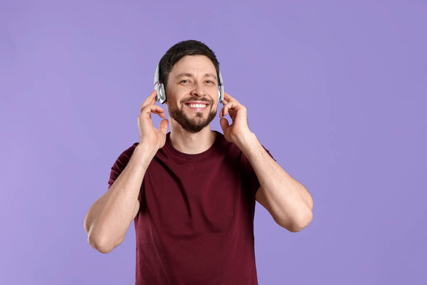 Happy man in headphones enjoying music on purple background - Фото, зображення