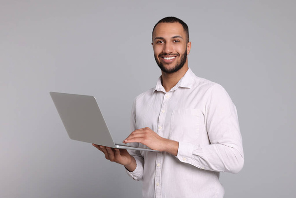 Smiling young man with laptop on grey background - Photo, image