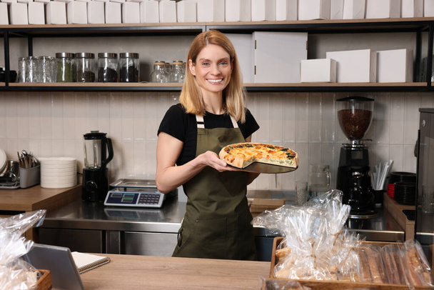 Happy seller holding delicious quiche at cashier desk in bakery shop - Photo, Image