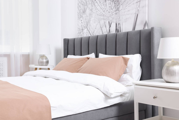 Comfortable bed and lamps on bedside tables in light room. Stylish interior - Zdjęcie, obraz