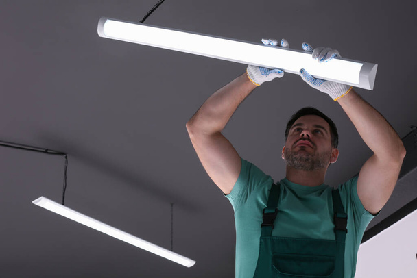 Ceiling light. Electrician installing led linear lamp indoors, low angle view - Fotografie, Obrázek