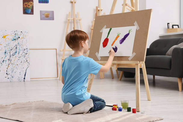 Little boy painting in studio. Using easel to hold canvas - 写真・画像