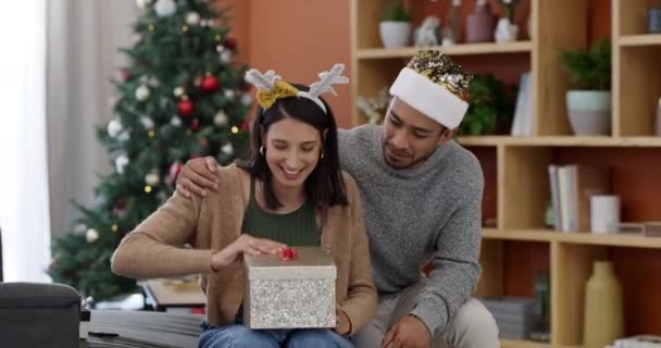 Χριστουγεννιάτικη έκπληξη, ζευγάρι και δώρο με ευτυχία και γιορτή στο σπίτι με καπέλο κόμμα. Ευτυχισμένος, δίνοντας δώρα και νέους ανθρώπους με το παρόν, κουτί και επικοινωνία σε ένα σαλόνι για διακοπές. - Πλάνα, βίντεο