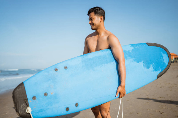 Smiling Asian man with surfboard on the beach enjoying beach vacation - Photo, image