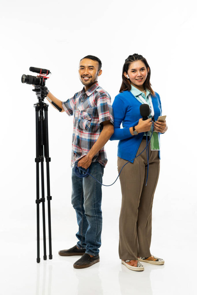 a beautiful reporter in blue cardigan and a cameraman with one set of camera standing back to back - Photo, Image