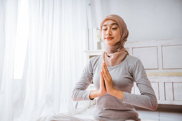 healthy muslim woman wearing hijab doing yoga pilates meditating in a room on orange mattress with eyes closed lotus pose in a room - Фото, зображення