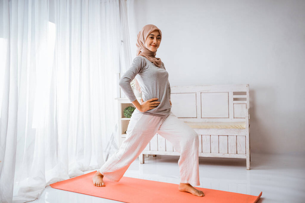 Müslüman tesettürlü kadın egzersizden önce ısınıyor. Bir odadaki yatakta mutlu bir şekilde çalışıyor. - Fotoğraf, Görsel