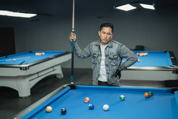 asian pool player put his hand on his waist while standing with sullen face and holding the cue stick - Photo, Image