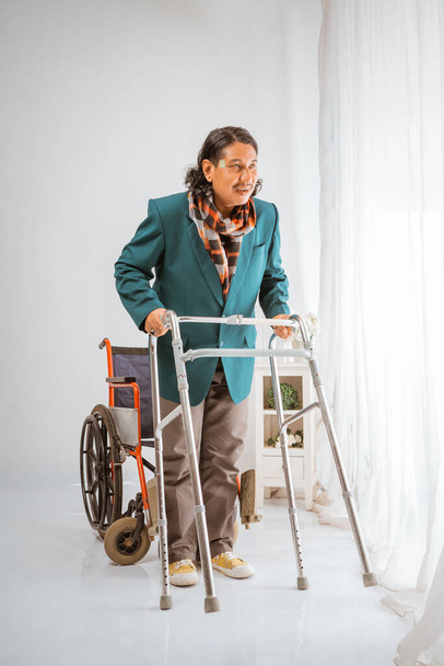 asian elderly man smiling standing in front of wheelchair trying to walk with walker frame happily in nursing home care - Photo, Image