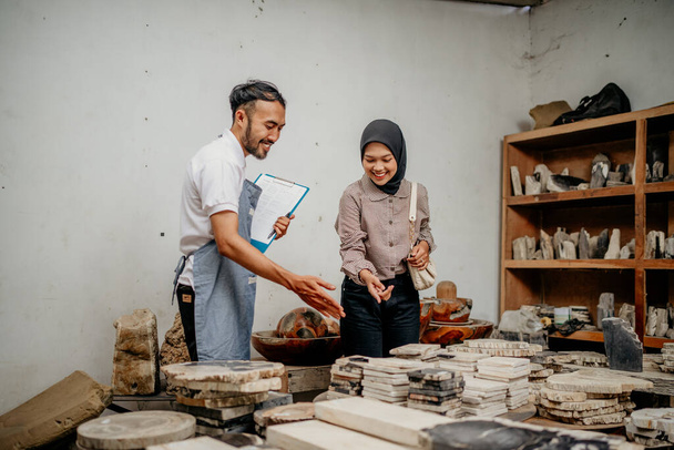 Male entrepreneur serving an Asian female customer by showing stone handicrafts at a stone craft shop - Photo, image