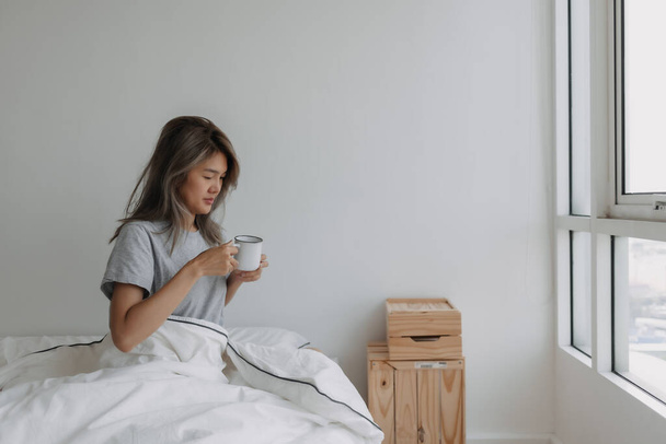 Asian woman drinking coffee right after wake up on the bed in the morning. - Zdjęcie, obraz