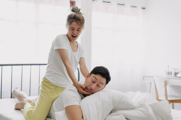 Funny asian couple wife giving husband hurt massage in white bedroom. - Photo, image