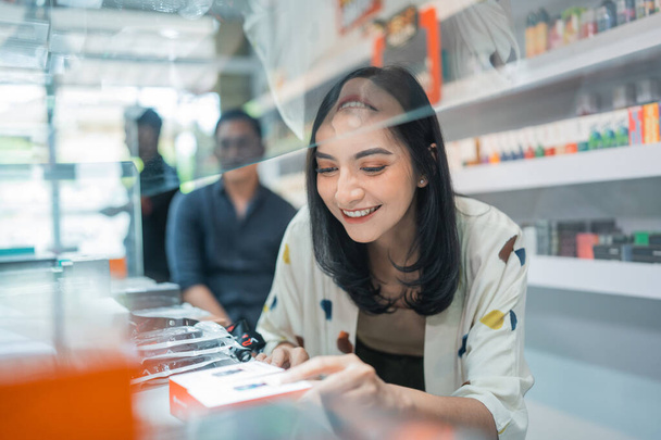 female seller smiling while picking the vape mod inside the display table - Fotografie, Obrázek