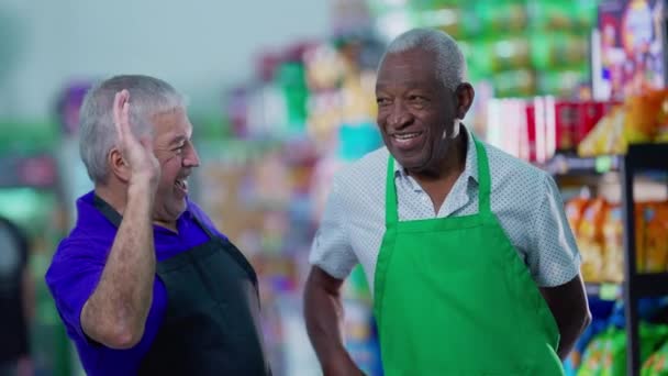Happy diverse senior employees celebrating success with high-five standing in supermarket aisle. Caucasian manager engaging with workforce teamwork with African American colleague - Footage, Video