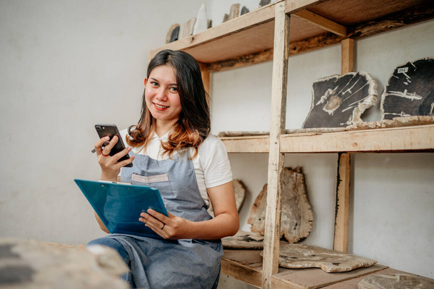 stone craft businesswoman smiles while holding a smartphone and clipboard in the warehouse - Фото, зображення