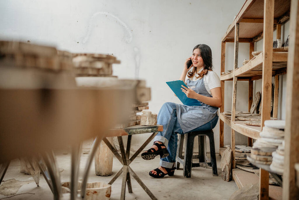 candid shot of a stone craft businesswoman making a phone call while holding a clipboard in a warehouse - Fotoğraf, Görsel