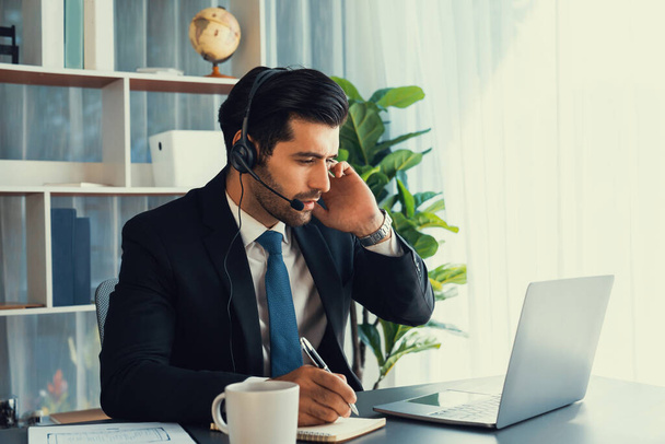 Male call center operator or telesales representative siting at his office desk wearing headset and engaged in conversation with client providing customer service support or making a sale. fervent - Foto, Imagen