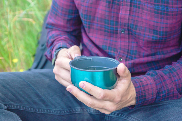 A thermo mug with a drink in the hands of a man. Active recreation in the park - Foto, Imagem