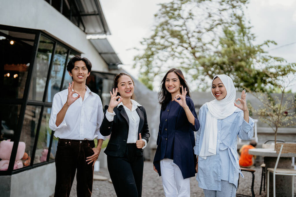 Group of cheerful young businesspeople wearing casual clothes with okay hand gestures standing in a coworking space - Foto, Bild